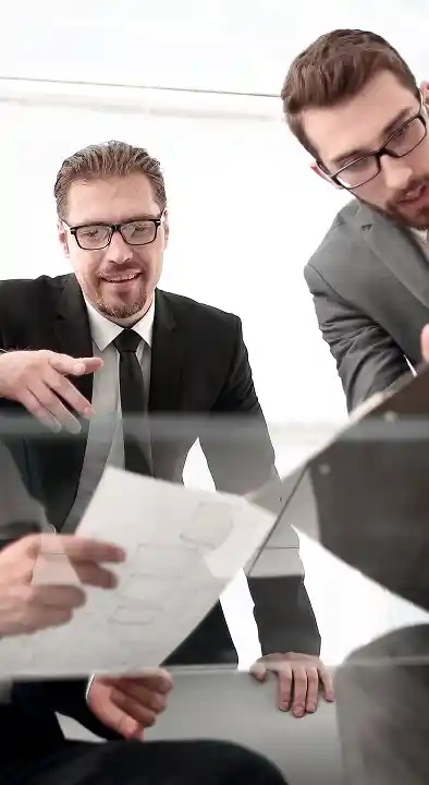 Vier mannen in pak werken samen op kantoor, terwijl ze documenten en een tablet doornemen. Ze zien er toegewijd en geconcentreerd uit en stralen teamgeest en professionaliteit uit.